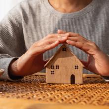 closeup-image-woman-protecting-covering-wooden-house-model-by-hands-with-warmness.